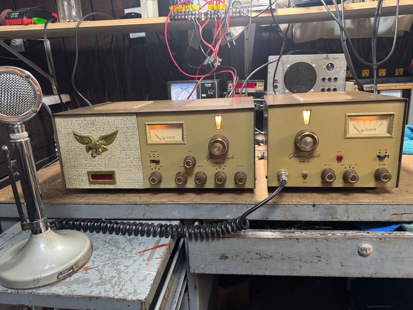 Two vintage radio receivers on a table with electronic equipment in the background.